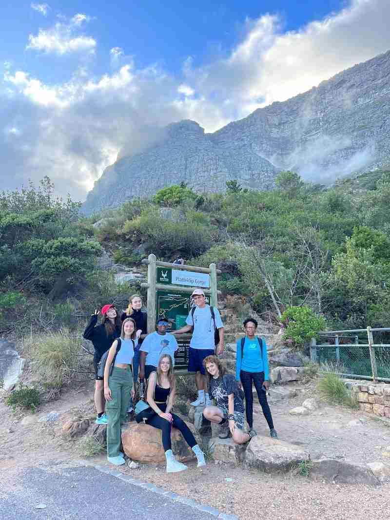 Excursie met vrienden naar de Platteklip Kloof Gemengde groep tieners op een wandeltocht voor een berglandschap en een bord met de tekst "Plattenkip Gorge".