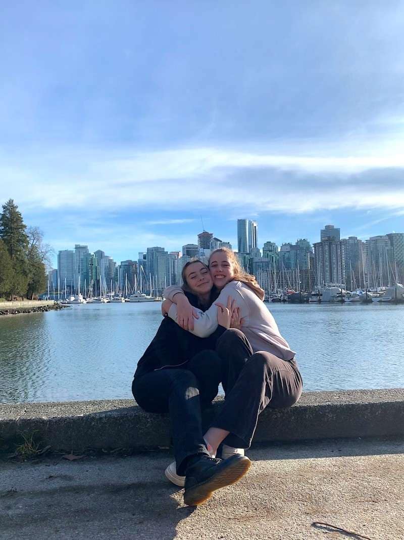 Isa with her friend in Canada Twee vrouwelijke tieners arm in arm zittend voor een meer met wolkenkrabbers op de achtergrond