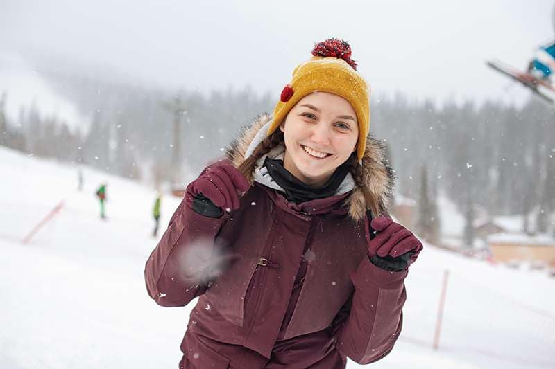 Into-Intercambio_estudiantil-Suecia Tienermeisje knielend op een heuvel in de sneeuw met een snowboard aan haar voeten