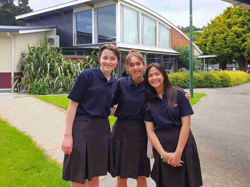 Meisjes in hun schooluniform in Nieuw-Zeeland Drie tienermeisjes in blauwe schooluniformen staan samen voor één huis