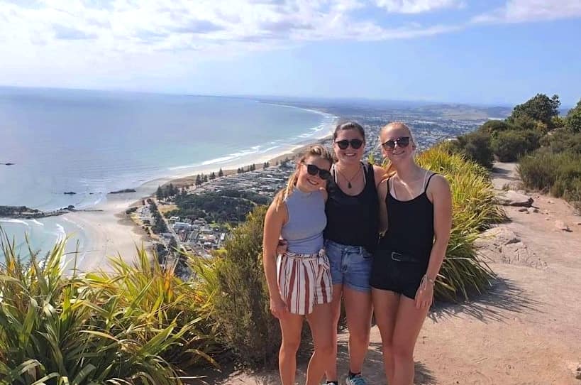 Into uitwisselingsstudent in Nieuw Zeeland met gastgezijg Vrouwelijke uitwisselingsstudent maakt een wandeling op een klif in Nieuw Zeeland met haar gastmoeder en gastzus